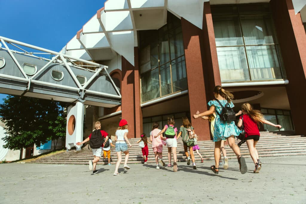 Happy kids playing at city's street in sunny summer's day in front of modern building. Group of happy childrens or teenagers having fun together. Concept of friendship, childhood, summer, holidays.